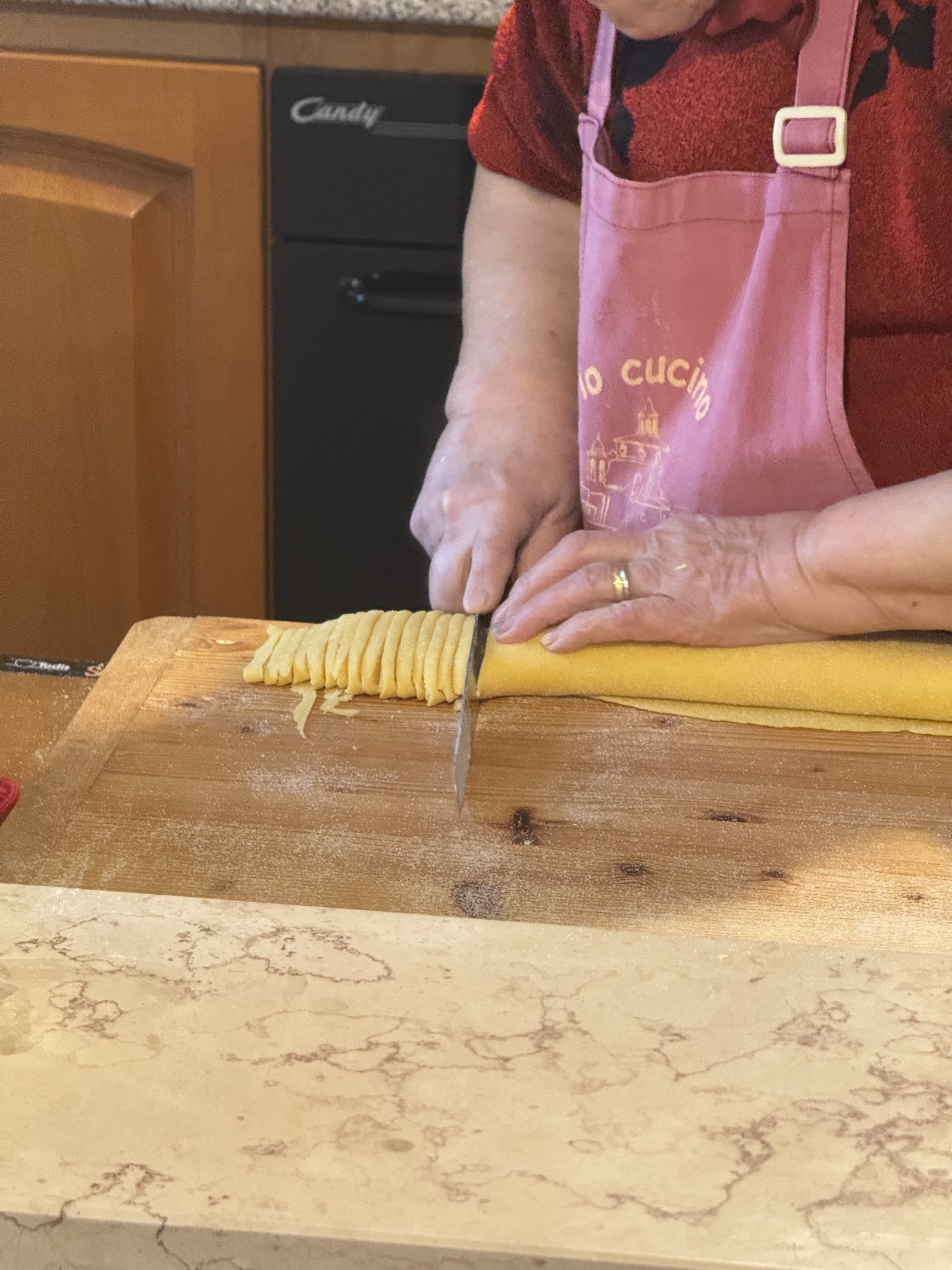 Le mani di zia Maria tagliano le fettuccine col coltello sul tagliere di legno